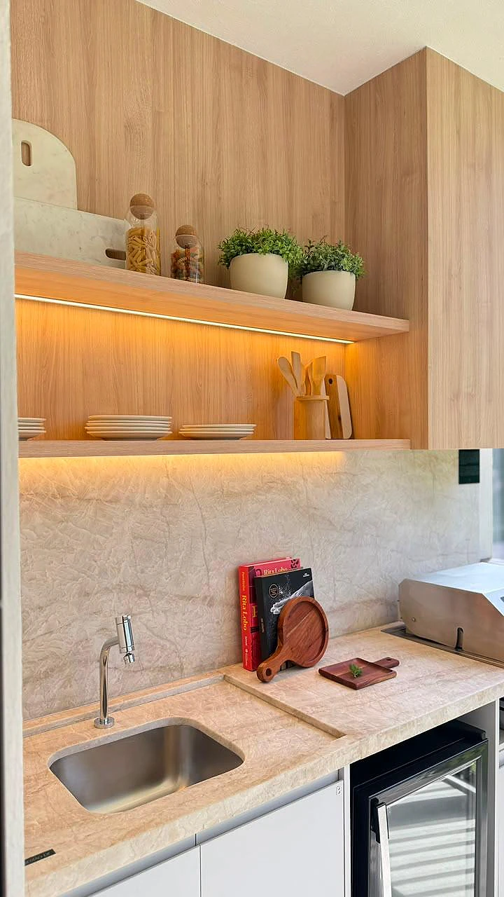 Bancada da varanda gourmet com prateleiras em madeira iluminadas e revestimento em pedra natural