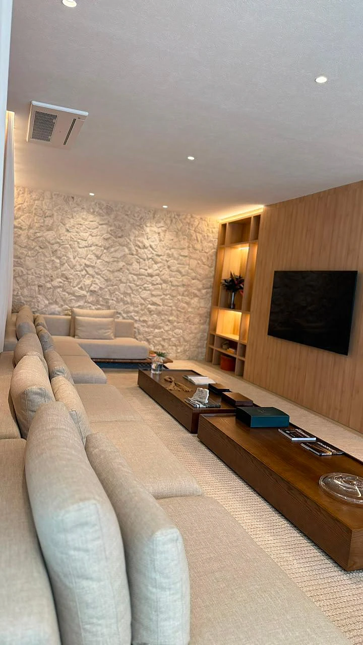 Living do decorado com sofá em L, parede de pedra, painel de madeira e estante iluminada