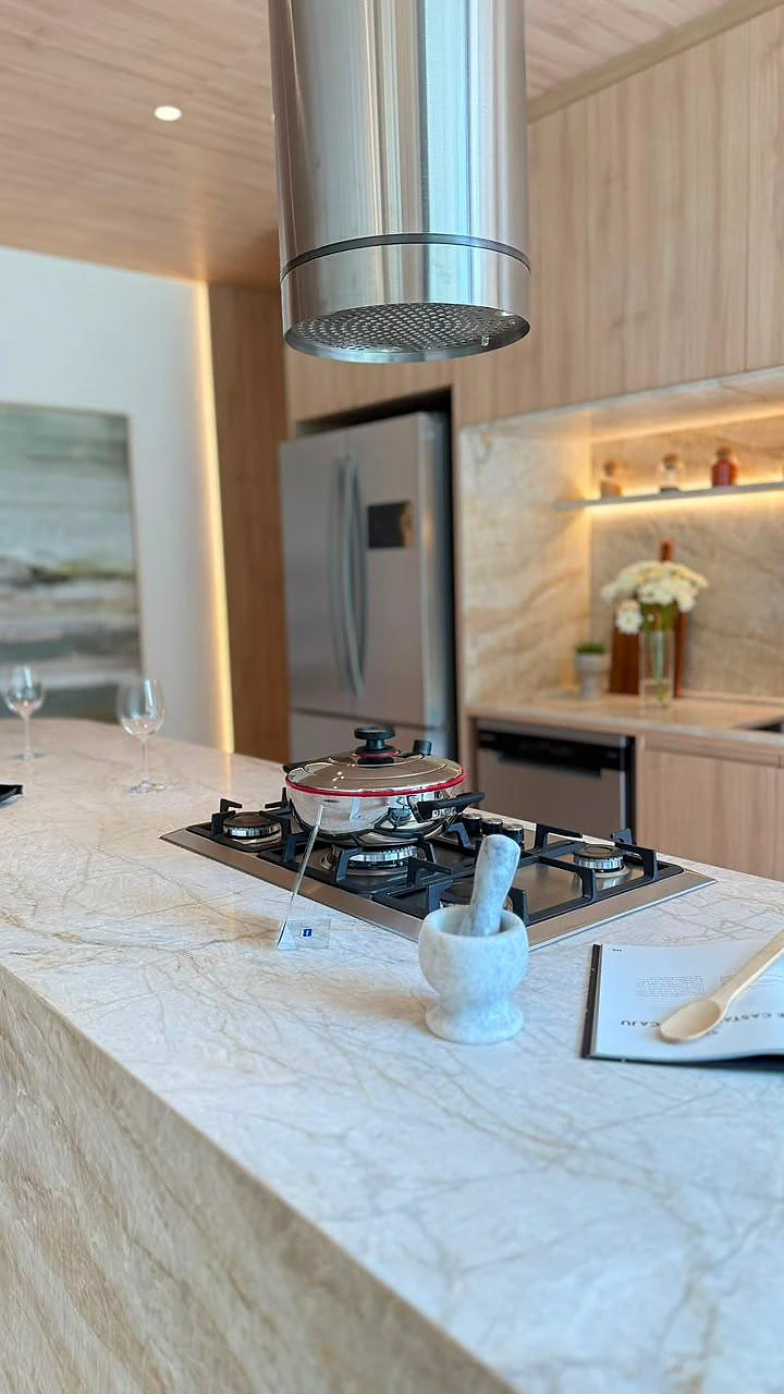 Ilha da cozinha em pedra natural com cooktop e coifa suspensa em inox