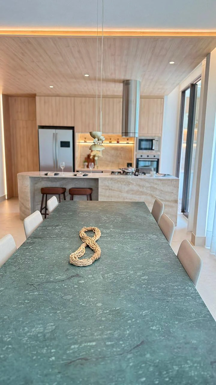 Mesa de jantar em pedra verde integrada à cozinha com ilha e marcenaria em madeira