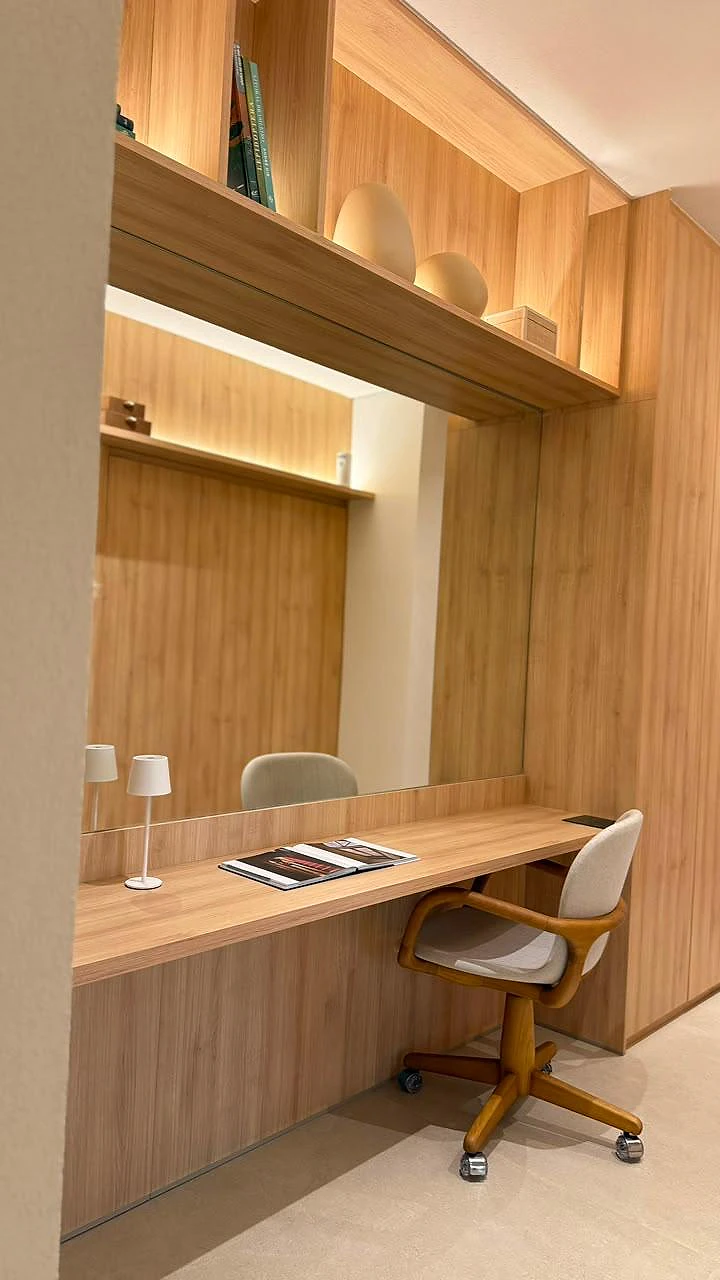 Home office com bancada em madeira, espelho e prateleiras iluminadas
