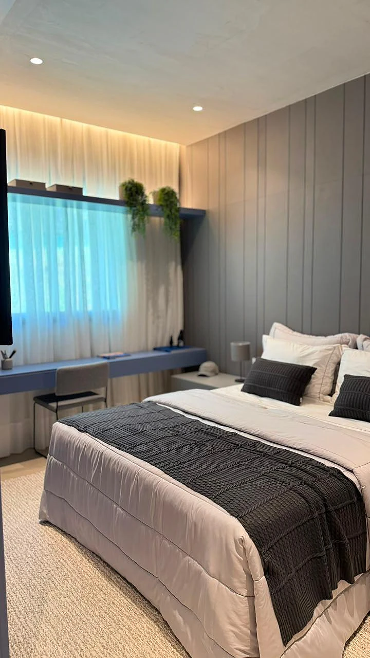 Suíte com cama de casal, painel ripado cinza e bancada de estudos junto à janela
