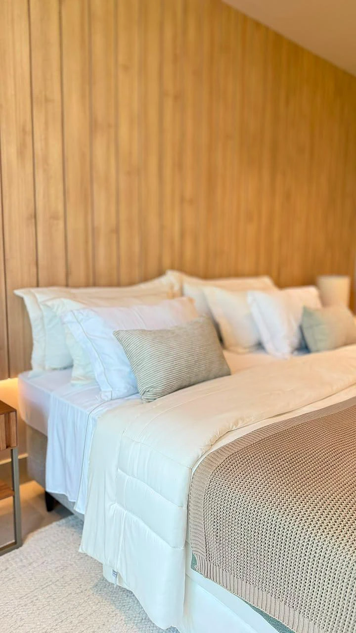 Detalhe da cama da suíte com cabeceira em painel de madeira ripada